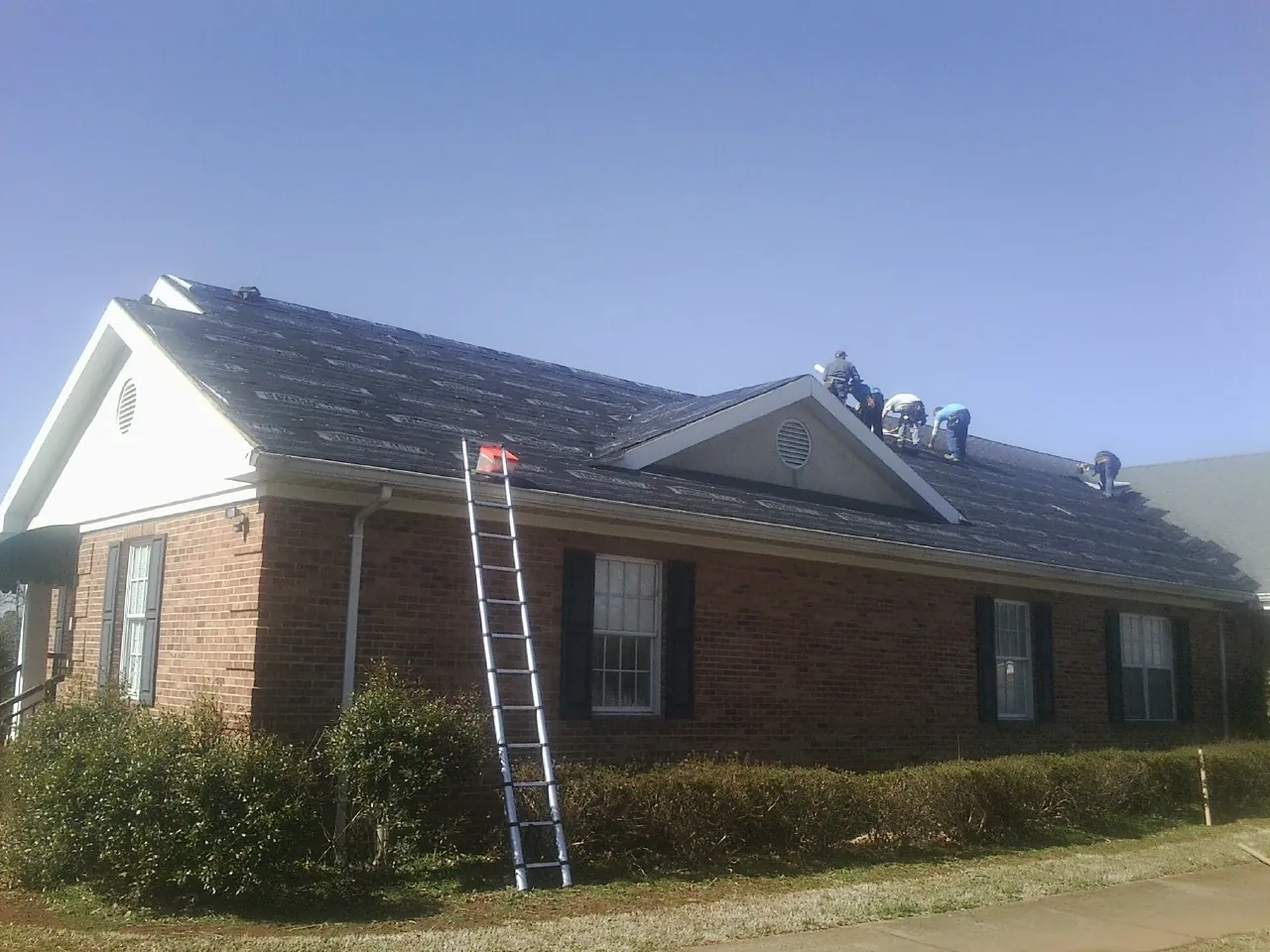Crew tearing shingles off a brick ranch roof with a ladder set — Metal Roof Repair work by our crew in Morrison