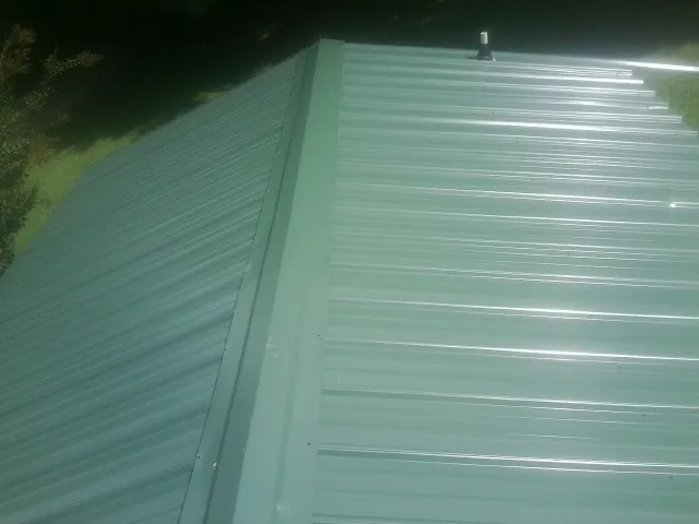 New green metal panels meeting at the ridge of a roof — Flat Roof Repair work by our crew in Morrison